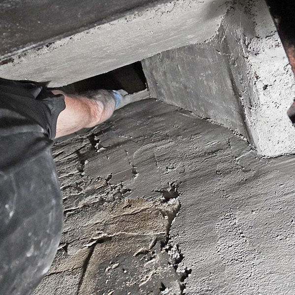 A chimney technician in Weymouth, MA applies mortar to the interior smoke chamber above a firebox, smoothing rough surfaces to improve draft and reduce fire risk.