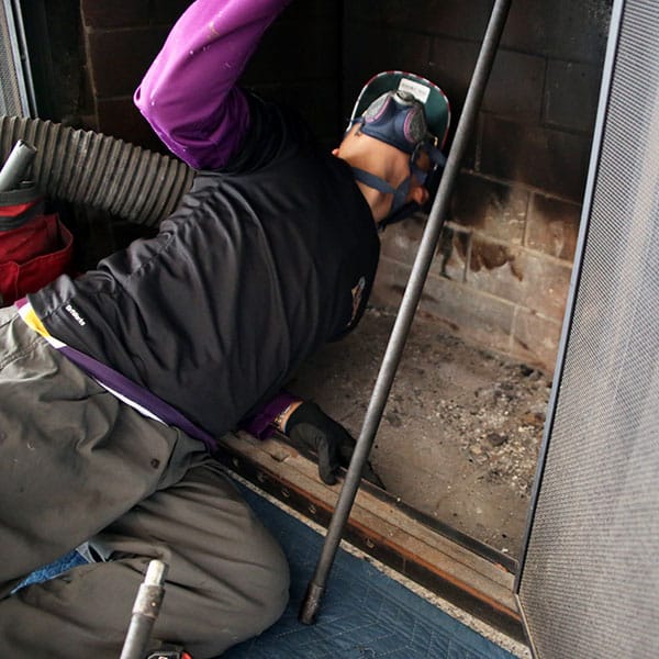 A chimney technician in Norwood, MA uses specialized brushes and a vacuum system to clean a masonry chimney flue, removing creosote buildup and soot to ensure safe fireplace use.