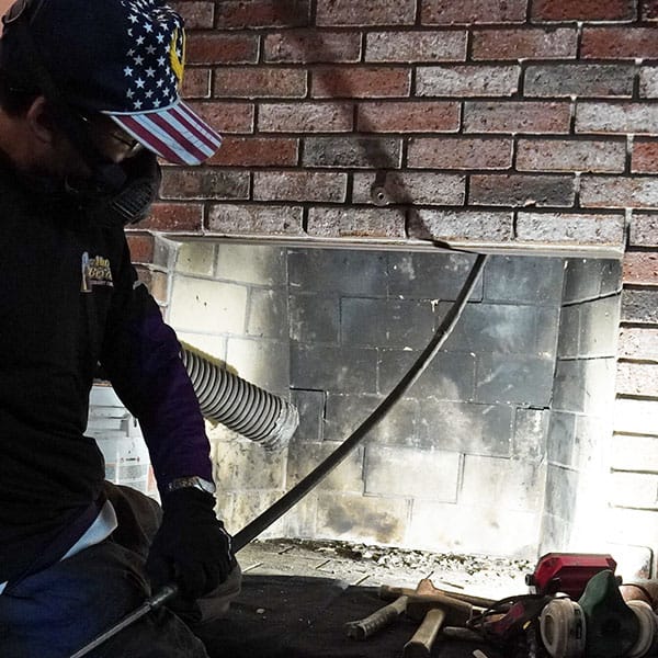 A certified chimney sweep in Pembroke, MA uses a rotary brush system and vacuum to remove soot and creosote from a residential fireplace and flue.