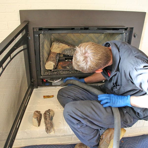 A certified technician in work gloves performs routine gas fireplace maintenance inside a Dedham, MA home, inspecting burner components and cleaning glass panels for safe and efficient heating.