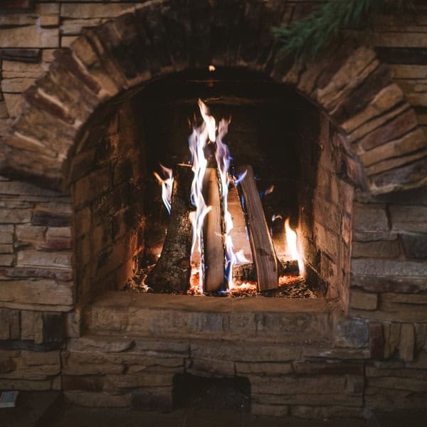 A cozy stone fireplace with burning logs and visible flames, surrounded by rustic stonework—perfect for relaxing evenings. Trust our chimney repair Norfolk and Plymouth County experts to keep your hearth safe and inviting.