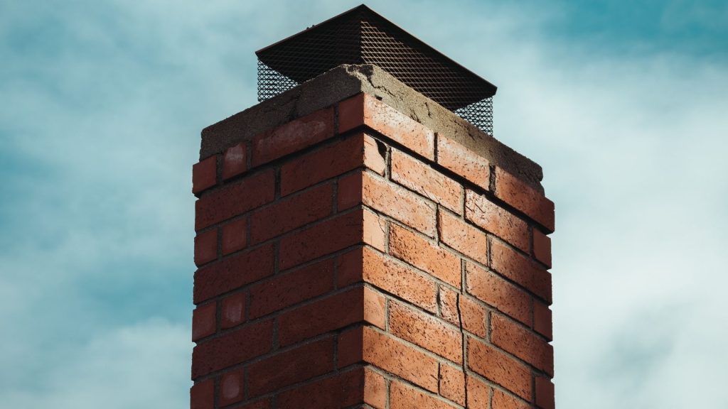 A close-up view of a red brick chimney with a metal cap against a partly cloudy blue sky, an example of quality chimney repair Norfolk and Plymouth County, MA residents can trust.