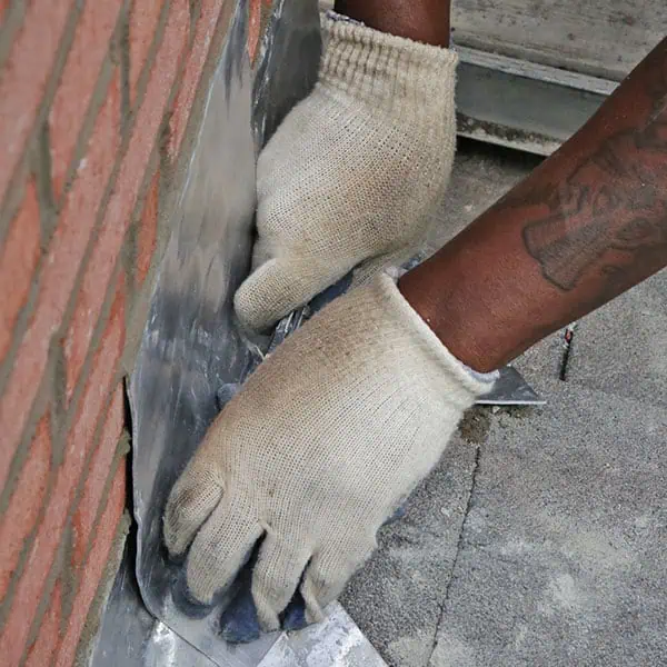 A person wearing white work gloves is installing or pressing metal flashing against a brick wall, likely as part of a chimney repair Norfolk and Plymouth County, MA project.