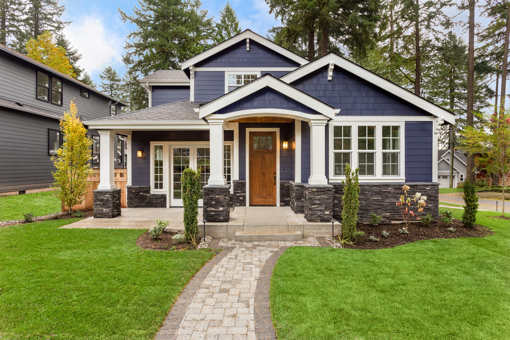 A modern two-story home in Massachusetts with navy blue siding, white trim, a wooden front door, stone accents, and a covered porch—featuring manicured landscaping and expert chimney repair in Norfolk and Plymouth County, MA.